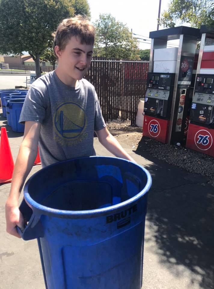 A student carrying a large recycling bin